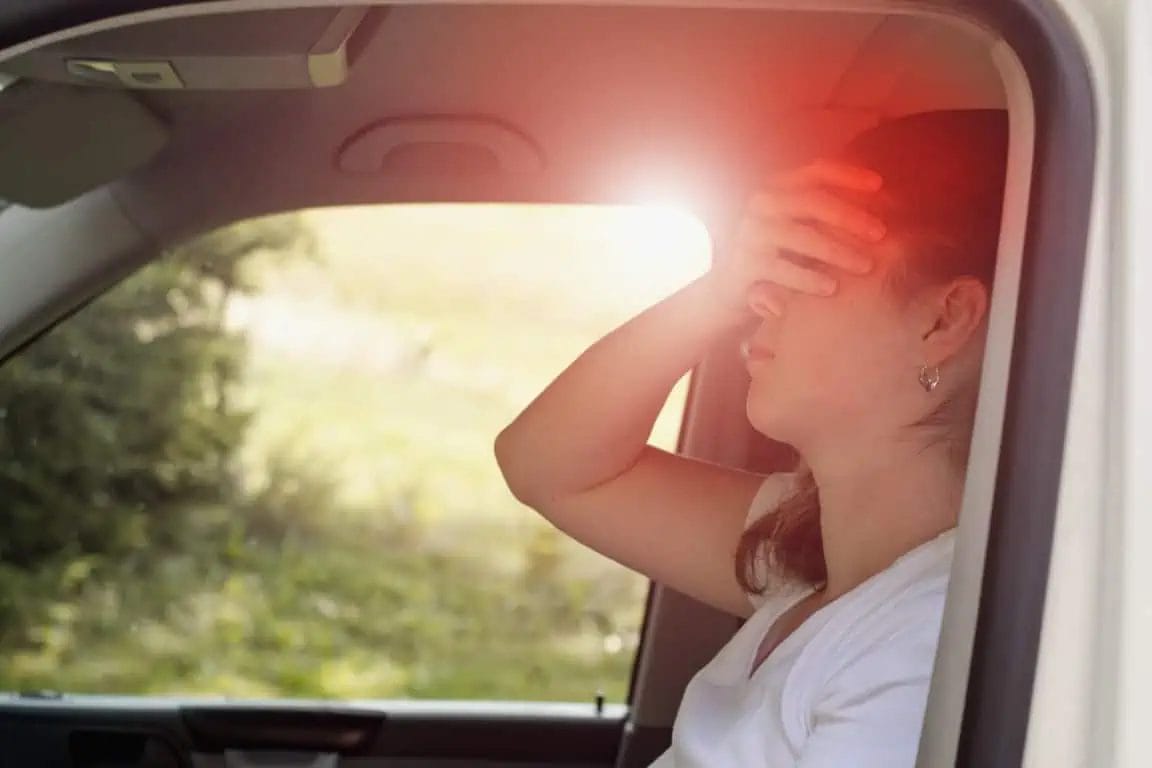 A woman sitting in car closing her eyes because of feeling motion sickness.