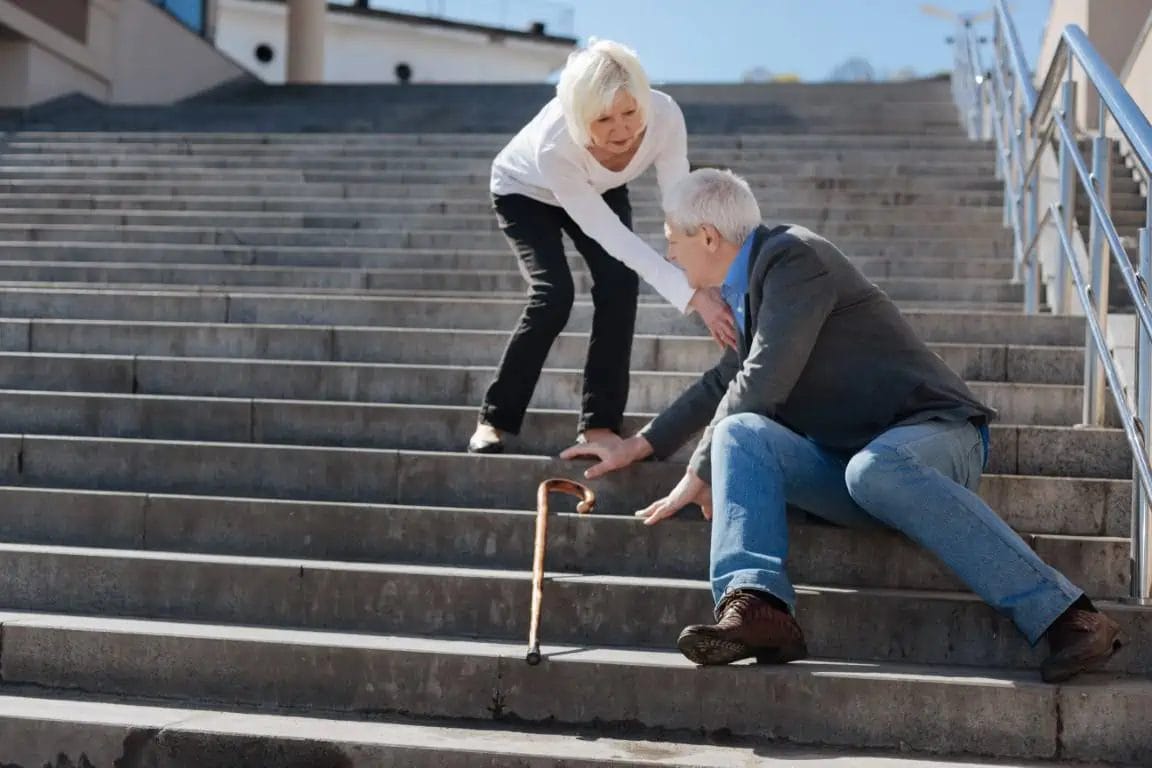 AN old person walking ion stairs fell down due to vertigo and another lady is helping him stand again