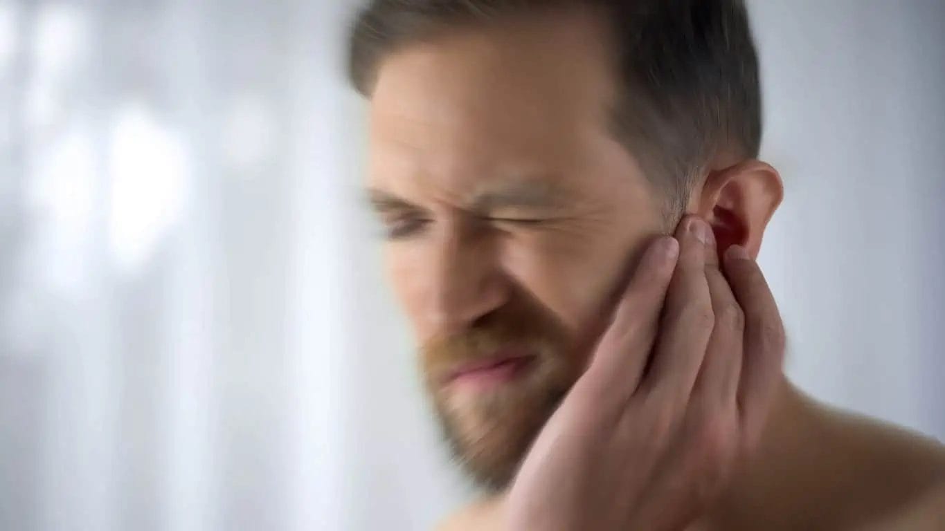 A person suffering from chronic tinnitus holding ears due to ringing sensation in ears.